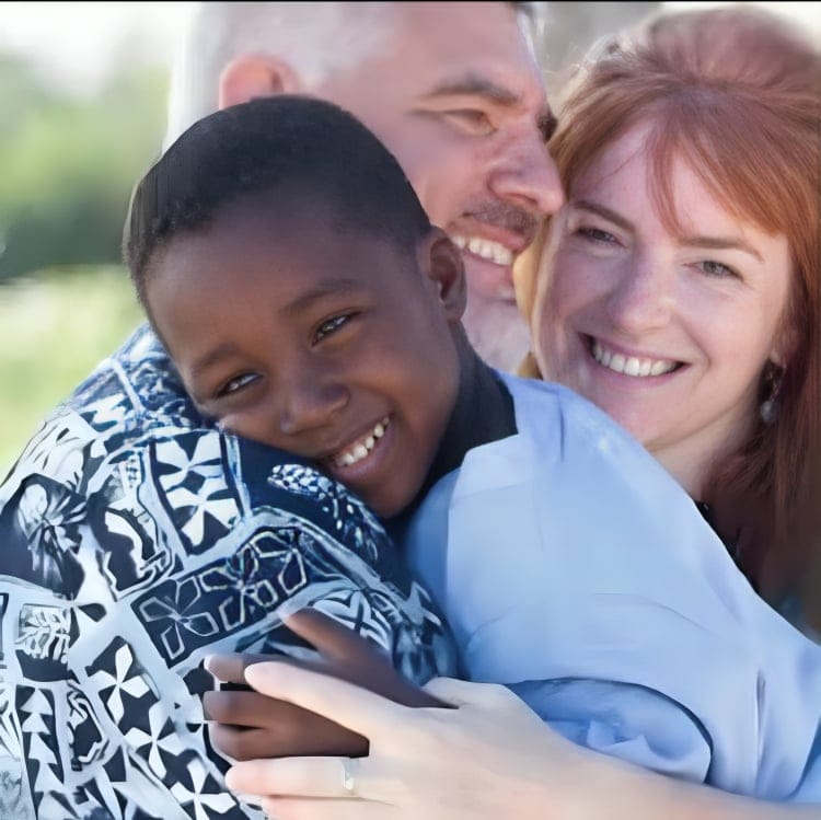 Un enfant souriant enlace deux adultes avec affection, tous les trois semblent heureux et complices en extérieur.